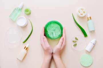 Woman hands holding aloe gel. Aloe vera leaves and cosmetic products on beige surface. Top view