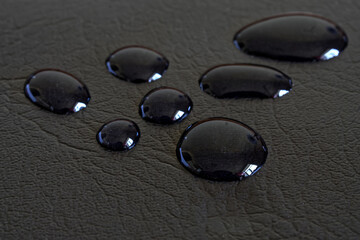 Dark water-repellent leather fabric of a jacket, raincoat or backpack, covered with drops of rain...