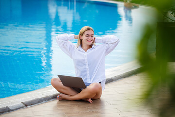 Young woman businessman with laptop sitting by the pool. Open workplace. Freelancer concept. Online shopping. Vacation work