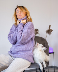 Young beautiful woman in sweater sitting on a chair with a white cute Pomeranian dog at home