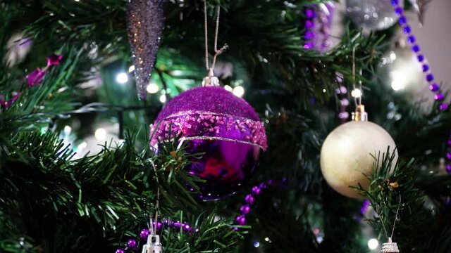 Close up on purple and white shimmering ball ornaments with illumination as background on a fir tree for New Year and Xmas. Lights of a Christmas tree glittering at night. 