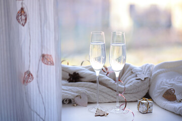 Two glasses of champagne and a gift on the windowsill decorated with Christmas tree wooden toys and pine cones.