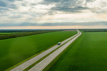Fototapeta premium green truck driving on asphalt road along the green fields. seen from the air. Aerial view landscape. drone photography. cargo delivery