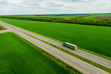 cargo delivery green truck driving on asphalt road along the green fields. seen from the air. Aerial view landscape. drone photography. © drotik