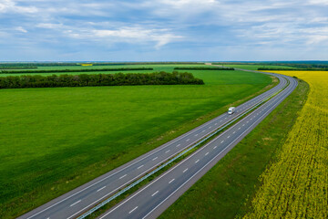 cargo delivery white truck driving on asphalt road along the green fields. seen from the air. Aerial view landscape. drone photography.