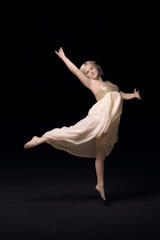 White girl dancing ballet on a black background. A young woman of European appearance froze in a jump. Ballet dance in white dress on black background. Ballerina soars in a jump