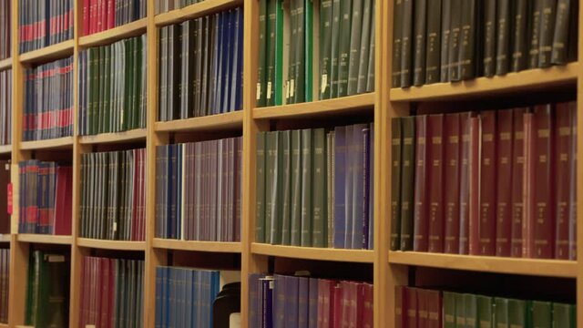 Slider dolly movement shot of books on rows of shelves in a research library, university, college, bookstore, or legal office.