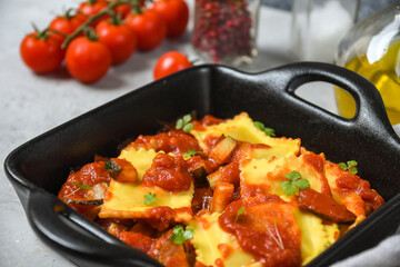 vegan ravioli tomato sauce on black pan on a wooden board. food delivery from restaurant to home.  top view, pasta recipe  Italian cuisine. Takeout coronavirus food. 