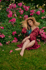 Romantic portrait of beautiful woman in red dress sitting in rose garden.