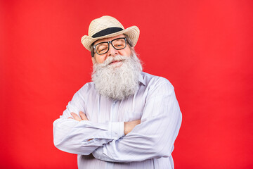 Charming handsome old aged senior man in casual shirt holding his arms crossed and smiling while standing isolated on red background.