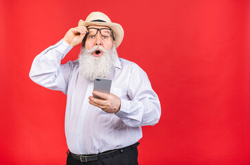 Old Senior shocked amazed Man dial phone number on smart phone, isolated on red background. Positive human emotion, facial expression. Using phone.