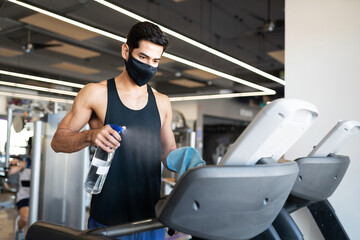 Male gym user cleaning a gym machine to prevent coronavirus