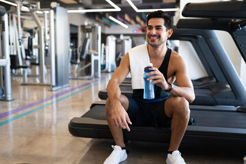 Happy young hispanic man sitting on a treadmill