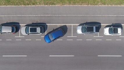 TOP DOWN: Flying above a shiny blue car driving out of a roadside parking space. - obrazy, fototapety, plakaty