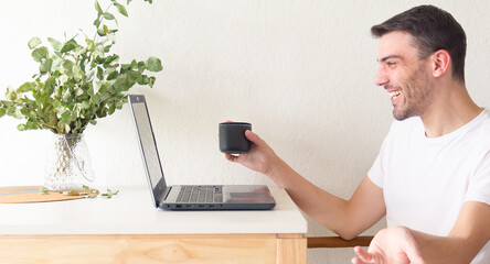 Retrato de un hombre adulto y apuesto caucásico sentado frente a su laptop y bebiendo una taza de...
