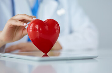 Female doctor with stethoscope holding heart, on light background