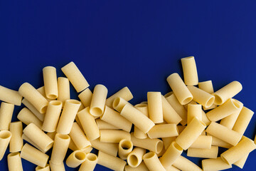 paccheri macaroni Italian dry raw pasta bronze drawn, pasta from Gragnano, on blue background top view
