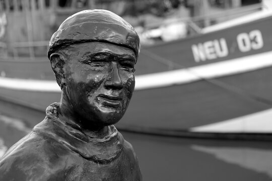 Skulptur des Altfischer mit altem Krabbenkutter im Hintergrund im Hafen von Neuharlingersiel an der K&uuml;ste der Nordsee bei Esens in Ostfriesland in Niedersachsen, fotografiert in Schwarzwei&szlig;