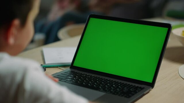 Unknown boy studying online at home. Kid using chroma key laptop indoors.