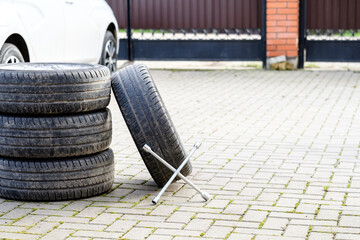 The wrench rests on the foot of the car wheels. An unknown white car on a blurred background. The concept of seasonal replacement of summer car tires with winter tires. Autumn day.