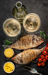Dinner for two. Grilled dorado fish with spices and a bottle of white wine with glasses on a stone background