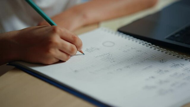 Schoolboy hand writing in notebook indoors. Unknown boy doing homework inside.