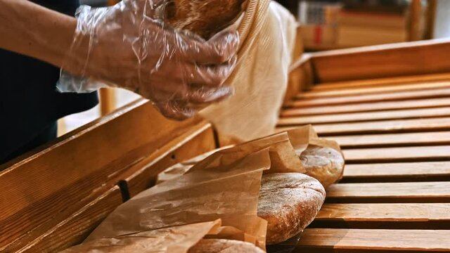 Man's hands taking bread from a wooden shelf and putting it in a reusable ecological bag in supermarket. Wearing plastic gloves. Ecology idea