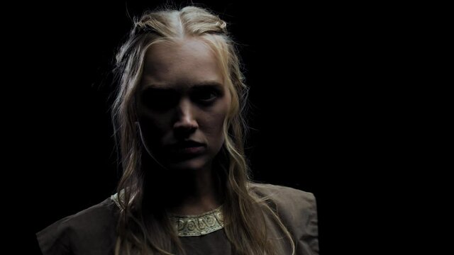 Blonde woman in medieval casual clothes is standing in a dark room, 4k