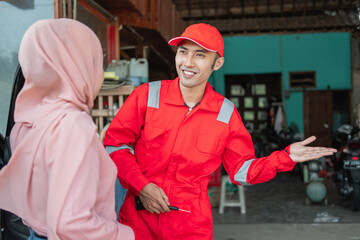 Asian car washer wearing red uniform standing smiling inviting customers to wait in the waiting room