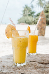 Pair of fruit shakes on the tropical beach. View of the beach and a surfboard