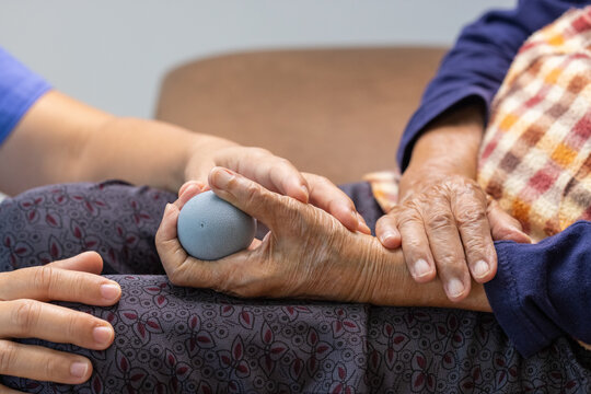 Elderly woman doing rubber ball for exercise fingers, palm ,hand and foot muscle with caregiver take care. - Powered by Adobe