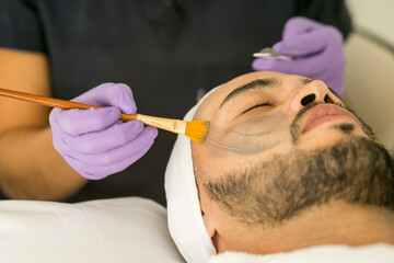 Limpieza facial de un hombre calvo en un spa, con fondo blanco y guantes morados