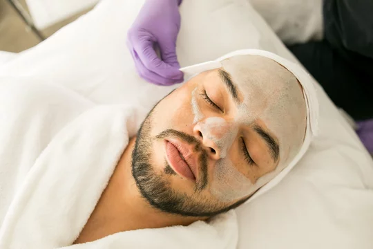 Limpieza facial de un hombre calvo en un spa, con fondo blanco y