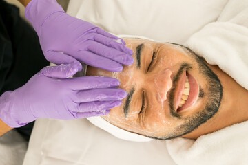 Limpieza facial de un hombre calvo en un spa, con fondo blanco y guantes morados
