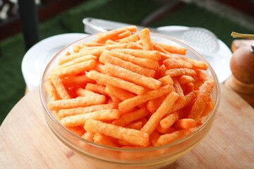pile of stick spicy corn chips in glass bowl on wooden background.