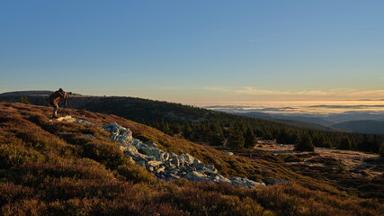 Photographer taking picture from a tripod from a mountain ridge during cloudless day on sunrise.