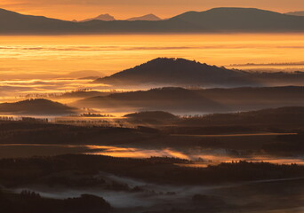 Sun light rays during sunshine peaking through morning mist on a wavy landscape.
