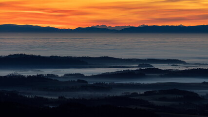 Obraz premium Silhouette of a church on a hill surrounded by morning mist and clouds during inversion sunshine in the morning with mountain ridge in the background.