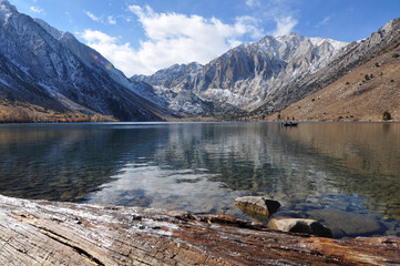 Pretty fall colors, snow-capped mountains, a big log, a fishing boat and reflections at Convict lake on a cloudy day in the autumn