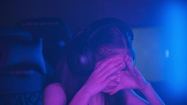Young attractive woman with light makeup sitting in neon gaming club - sad sighing and holding her head