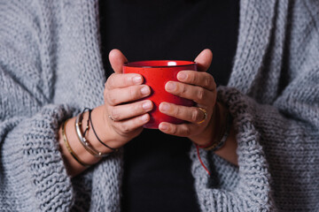 Closeup of a woman's hands with a red mug. Woman warming her hands with a cup of coffee