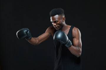 Plakat Young African American Boxer wearing gloves is posing isolated on a dark background