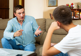Angry adult man scolding his offended young son in living room