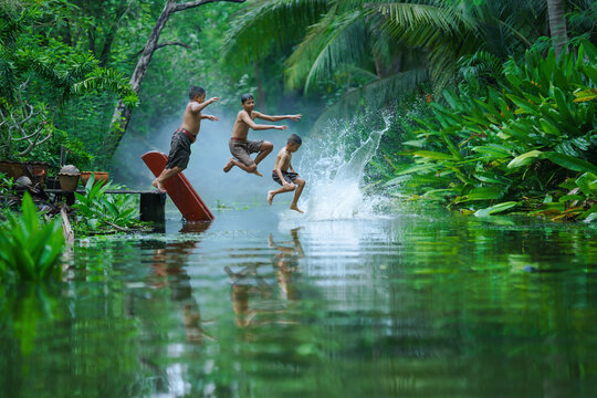 three local thai boys enjoying jumping water in canal together