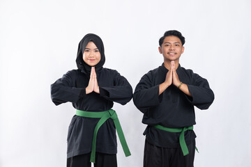 Hooded women and men in pencak silat uniform poses respectfully with both hands cupped in front of chest in isolated background