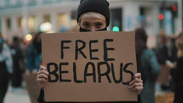 Young woman with face mask holding banner with writtings - free belarus. High quality 4k footage