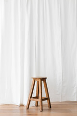 Wooden stool in front of a white curtain