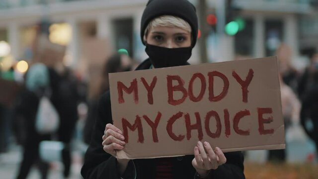 Woman holding a sign My Body, My Choice. Protest against tightening of the abortion law . Nationwide women's strike. Wearing protective face mask against COVID-19 Coronavirus. High quality 4k footage