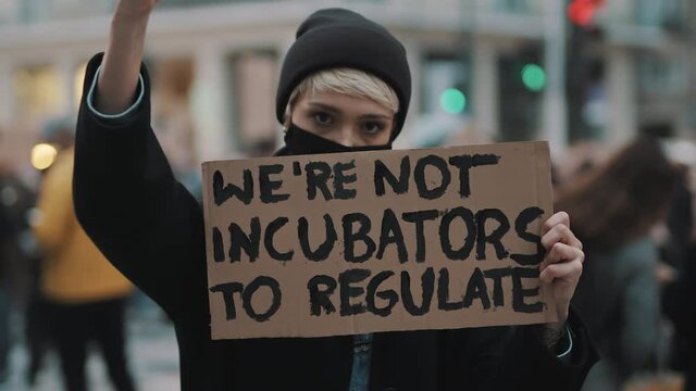 Womens march. Young woman with face mask protesting with banner sign - We are not incubators to regulate. protest against strict abortion laws. High quality 4k footage
