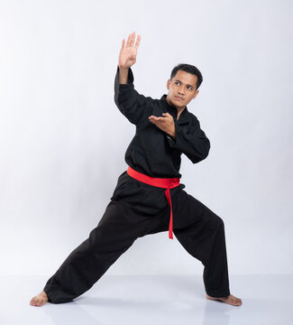 Asian male poses with pencak silat moves while wearing a pencak silat uniform on a white background